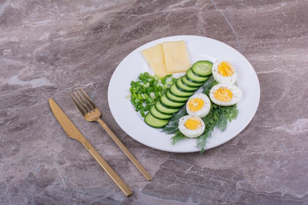eggsufs durs avec des tranches de concombres et d'herbes dans une assiette blanche.