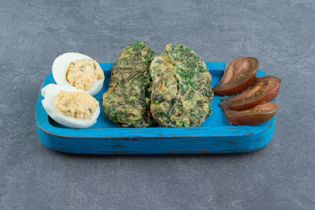 egguf à la coque et œuf au plat avec des verts sur plaque bleue.