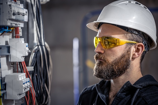 Un électricien de sexe masculin travaille dans un standard avec un câble de raccordement électrique.