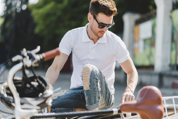 Photo gratuite Élégant jeune homme réparant le vélo sur route