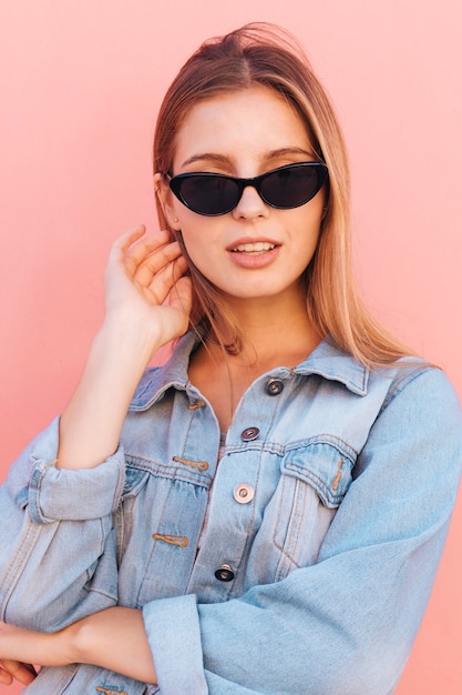 Photo gratuite Élégante jeune femme en chemise en jean bleu debout sur fond rose