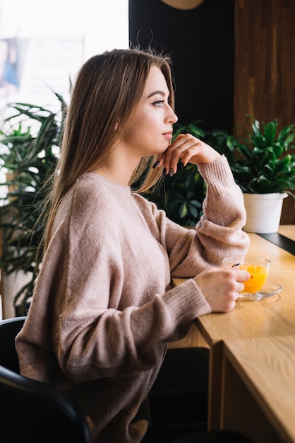 Photo gratuite Élégante jeune femme réfléchie avec une tasse de boisson au comptoir au café