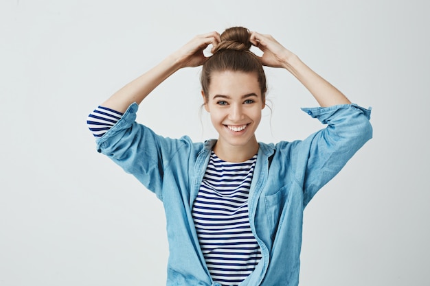 L'élève est prêt à commencer à travailler sur sa peinture. Portrait de la belle fille heureuse faisant la coiffure chignon, tirant les cheveux avec les mains et souriant largement. permanent