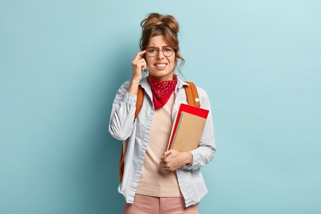 Un élève fatigué insatisfait garde le doigt sur la tempe, a mal à la tête après de longues études, tient un journal et un manuel