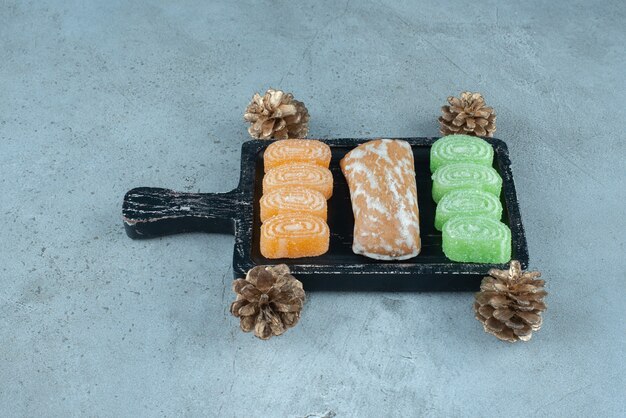 Emballage de biscuits et bonbons à la gelée sur un petit plateau au milieu de pommes de pin sur une surface en marbre