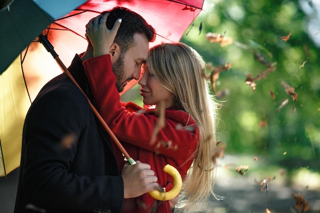 Embrasser un couple d'amoureux sous un parapluie coloré dans le parc. Passer du temps ensemble. Notion d'amour.