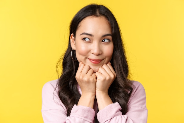 Les émotions des gens, les loisirs de style de vie et le concept de beauté. Une fille asiatique rêveuse et idiote a une idée intéressante en tête, imaginant quelque chose comme regardant à gauche et souriant, plan intrigant, fond jaune.