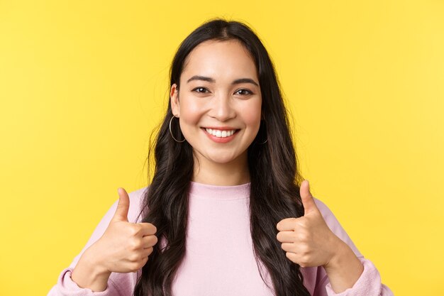 Les émotions des gens, les loisirs de style de vie et le concept de beauté. Fille asiatique souriante optimiste montrant le pouce levé en signe d'approbation, fond jaune debout, idée d'accord et de soutien, fond jaune.