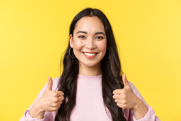 Les émotions des gens, les loisirs de style de vie et le concept de beauté. Fille asiatique souriante optimiste montrant le pouce levé en signe d'approbation, fond jaune debout, idée d'accord et de soutien, fond jaune.