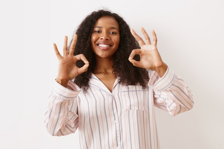 Photo gratuit émotions humaines positives, sentiments et expressions faciales. jolie fille africaine joyeuse avec une coiffure volumineuse et un large sourire radieux, montrant un geste correct, reliant le pouce et l'index