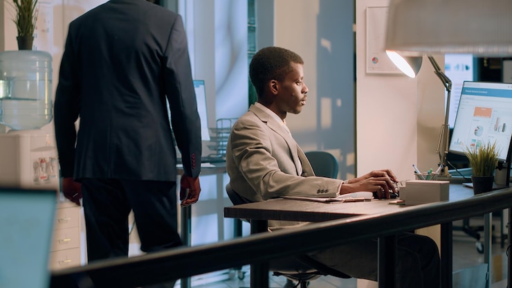 Photo gratuit employé afro-américain croisant des chiffres financiers entre des tableaux et des diagrammes sur l'écran d'ordinateur pendant la nuit. travailleur efficace comparant les chiffres de l'entreprise au bureau.