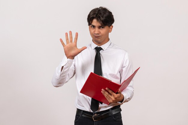 Employé de bureau masculin de vue de face tenant le dossier rouge sur le travail humain de bureau de travail de mur blanc