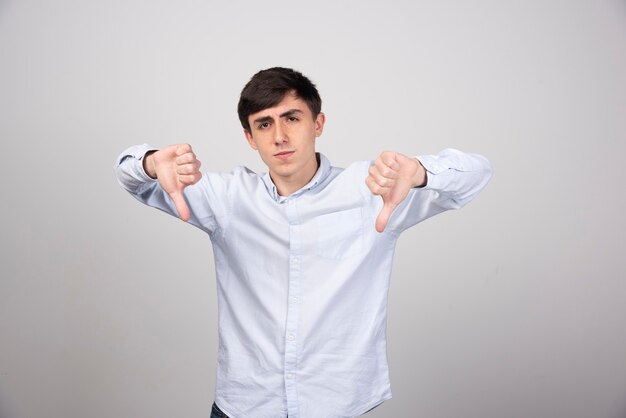 employé de bureau en tenue de soirée montrant les pouces vers le bas sur un mur gris.