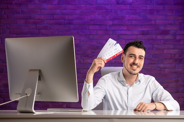 Employé de bureau vue de face assis derrière son lieu de travail et tenant des billets d'avion