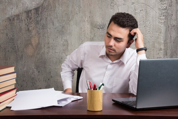 Employé fatigué assis au bureau et regardant sur des feuilles de papier. Photo de haute qualité