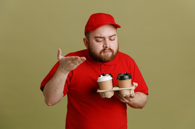 Employé de livreur en uniforme de t-shirt blanc à capuchon rouge tenant des tasses à café inhalant un arôme agréable debout sur fond vert