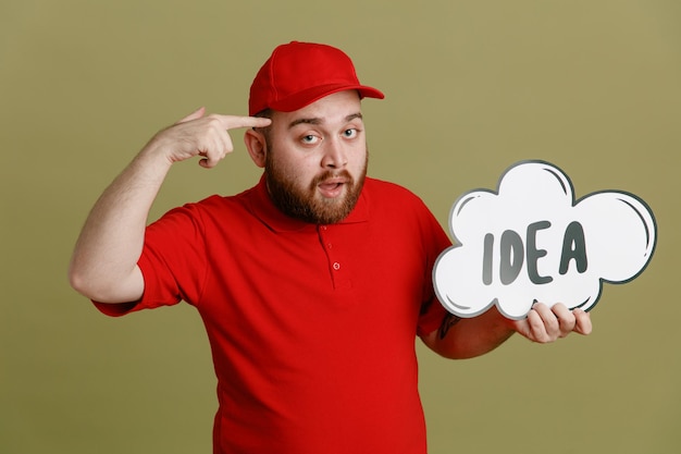 Employé de livreur en uniforme de t-shirt blanc à casquette rouge tenant un discours de bulle avec une idée de mot regardant la caméra pointant avec l'index sur sa tête debout sur fond vert