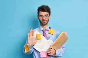 Photo gratuite un employé masculin sérieusement battu dit que le maintien tire la paume vers la caméra dans un geste d'arrêt regarde avec une expression stricte refuse votre aide prépare le travail du projet par lui-même habillé formellement