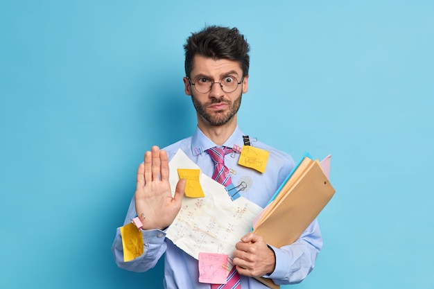 Un employé masculin sérieusement battu dit que le maintien tire la paume vers la caméra dans un geste d'arrêt regarde avec une expression stricte refuse votre aide prépare le travail du projet par lui-même habillé formellement