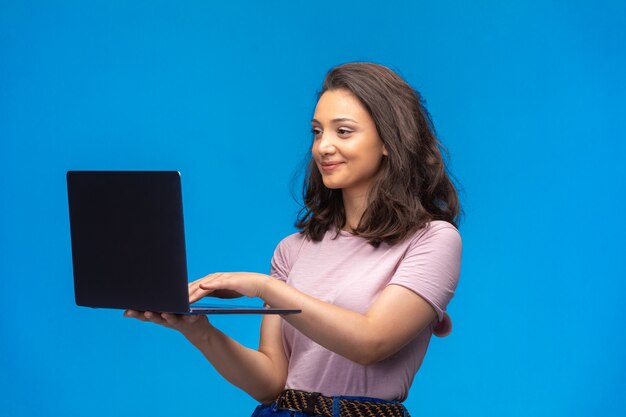 Employé de sexe féminin avec un ordinateur portable noir ayant un appel vidéo sur le mur bleu