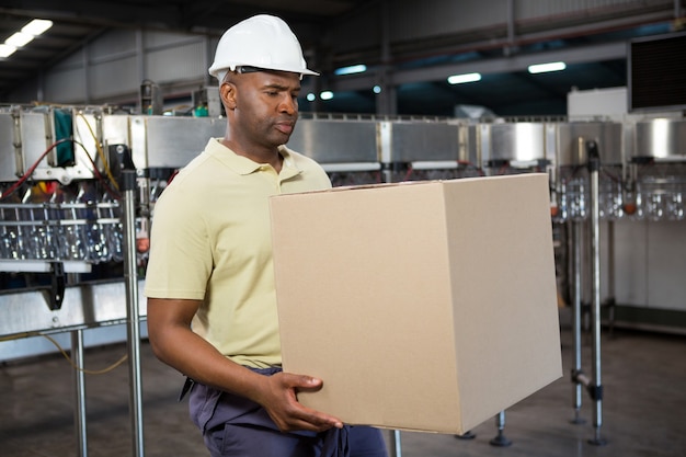 Employé de sexe masculin transportant une boîte en carton dans l'usine de jus