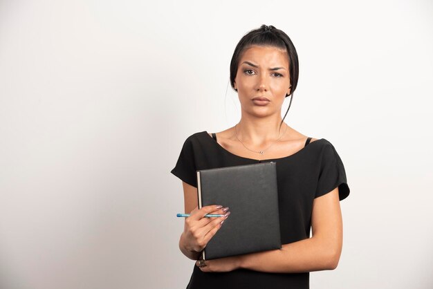 Employée brune avec ordinateur portable posant sur un mur blanc.
