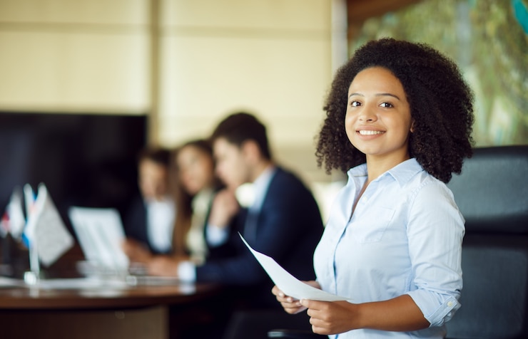 Photo gratuit employée heureuse et souriante avec ses collègues dans une ombre floue derrière