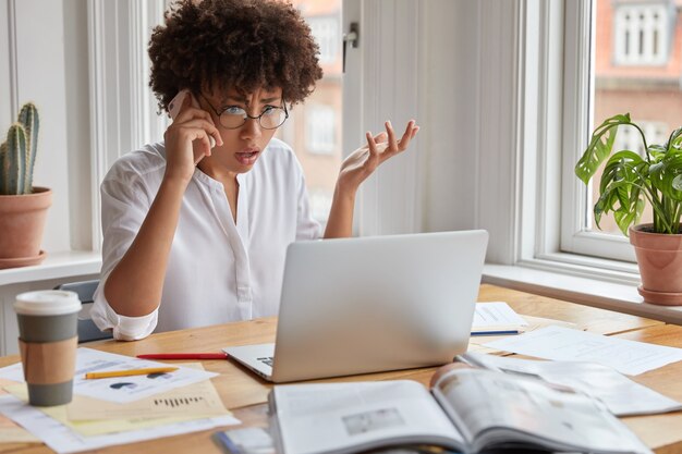 Une employée indignée et choquée, perplexe, hausse les épaules de frustration, regarde un ordinateur portable, vérifie la base de données