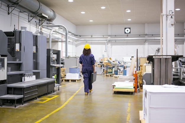 Employée industrielle afro-américaine en casque et en général marchant sur le sol de l'usine