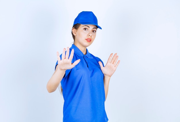 Employée de livraison en uniforme bleu debout et montrant un panneau d'arrêt.