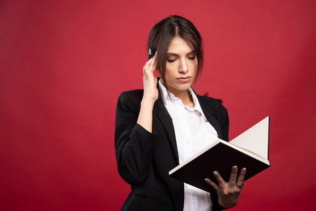 Employée réussie lisant son livre de mémoire sur fond rouge.