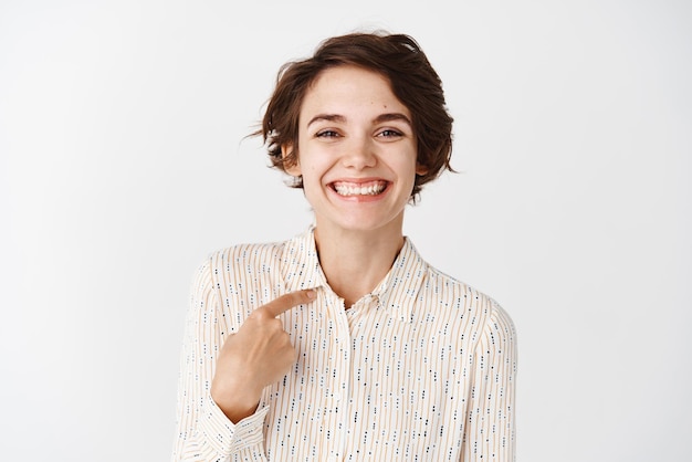 Une employée souriante qui a l'air heureuse de se pointer du doigt debout dans un chemisier décontracté sur fond blanc Copier l'espace