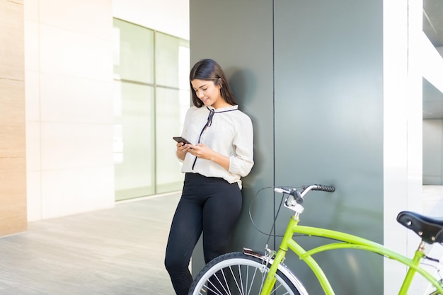 Employée utilisant des applications mobiles en vélo vert contre colonne