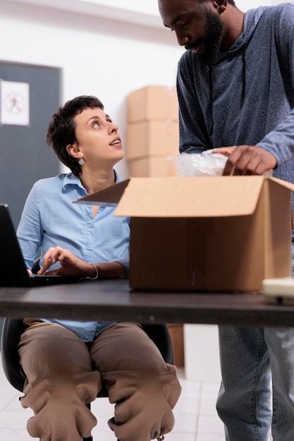 Photo gratuite employés de l'entrepôt préparant les colis des clients mettant la commande dans une boîte en carton enveloppée de papier bulle tout en discutant des détails d'expédition, équipe diversifiée travaillant dans le service de livraison de l'entrepôt