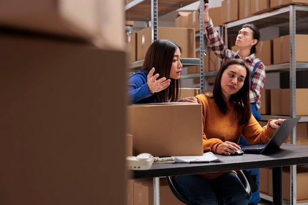 Photo gratuite les employés de l'entrepôt vérifient la satisfaction des clients en matière de livraison sur un ordinateur portable et discutent des commentaires négatifs. des collègues asiatiques du service postal gèrent l'expédition à partir d'un ordinateur d'entrepôt