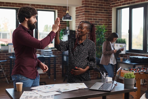 Les employés de l'entreprise de marketing se félicitent pour les excellents résultats de la stratégie de marketing de démarrage. Heureuse femme enceinte souriante collègue de haut cinq pour des idées de présentation incroyables.