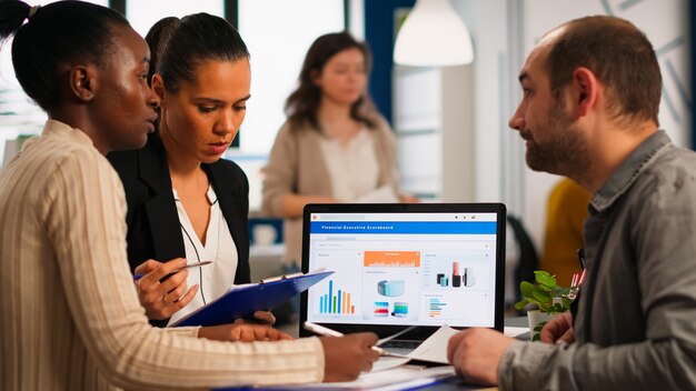 Employés multiculturels et diversifiés occupés à analyser les statistiques financières annuelles, assis au bureau devant un ordinateur portable contenant des documents à la recherche de solutions commerciales. Équipe d'hommes d'affaires travaillant en entreprise