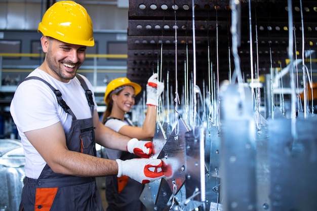 Employés d'usine avec des casques jaunes inspectant les pièces métalliques dans l'usine automobile