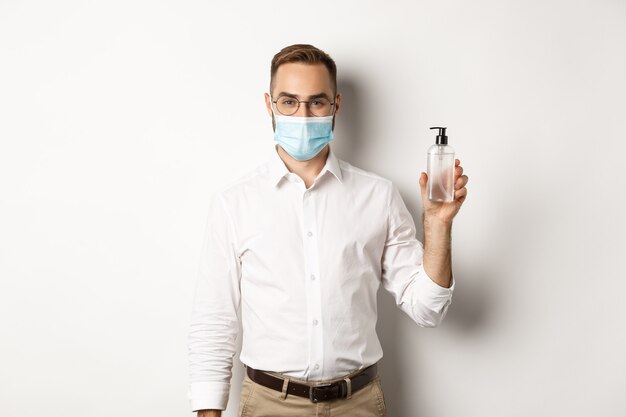 Employeur en masque médical montrant un désinfectant pour les mains, demandant d'utiliser un antiseptique au travail, debout