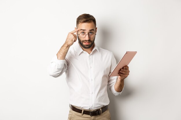 Employeur mécontent qui gronde le personnel tout en vérifiant le rapport sur la tablette numérique, pointant la tête et l'air déçu, debout