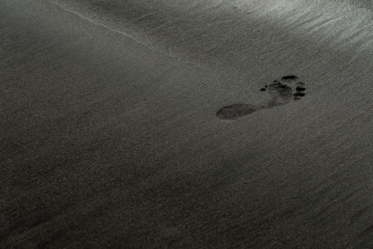 Photo gratuit empreinte sur une macro photographie de plage de sable noir. trace humaine sur une texture de plage noire et soyeuse avec une faible profondeur de champ. fond noir minimaliste. ténérife rivage sablonneux voulcanic.