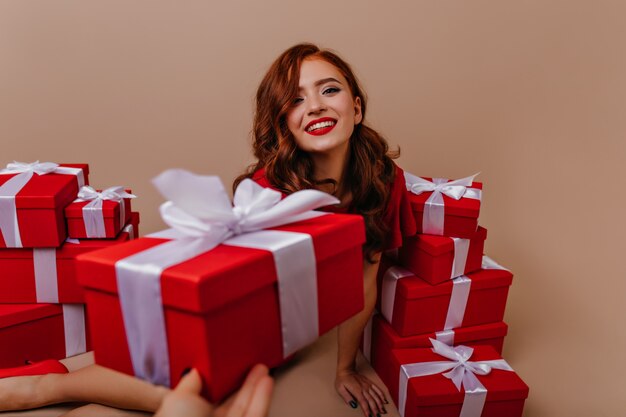 Enchanteur femme aux cheveux longs posant à côté des cadeaux de Noël. Fille de gingembre romantique appréciant la fête du nouvel an.