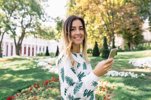 Enchanteur femme bronzée regarde à l'avant avec un sourire inspiré tout en marchant dans le parc