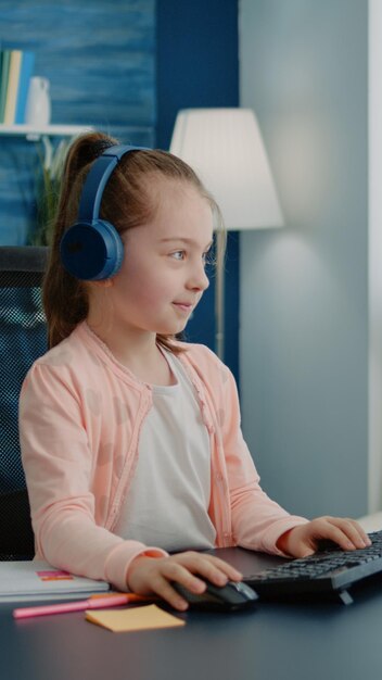 Enfant agitant à la webcam d'appel vidéo sur ordinateur pour le travail scolaire au bureau. Jeune fille utilisant une conférence en ligne pour une leçon en classe et apprenant à la maison. Élève avec un casque sur internet