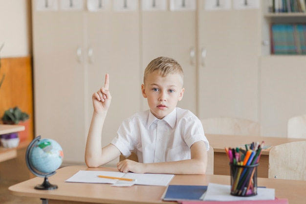 Enfant assis au bureau dans la salle de classe en levant la main