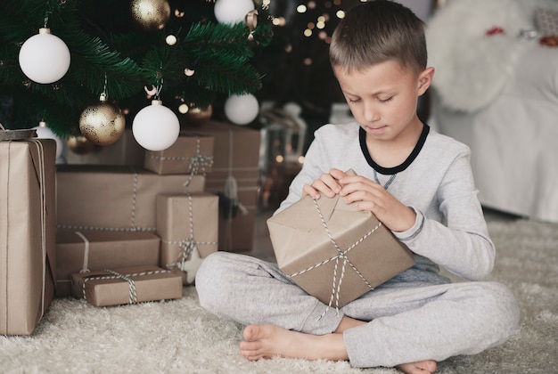 Enfant aux pieds nus en pyjama ouvrant un cadeau sur le sol