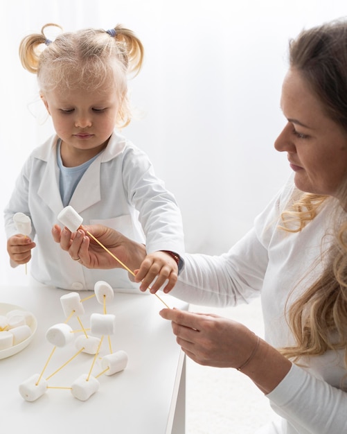 Photo gratuite enfant en bas âge mignon et femme apprenant la science avec des guimauves et des pâtes