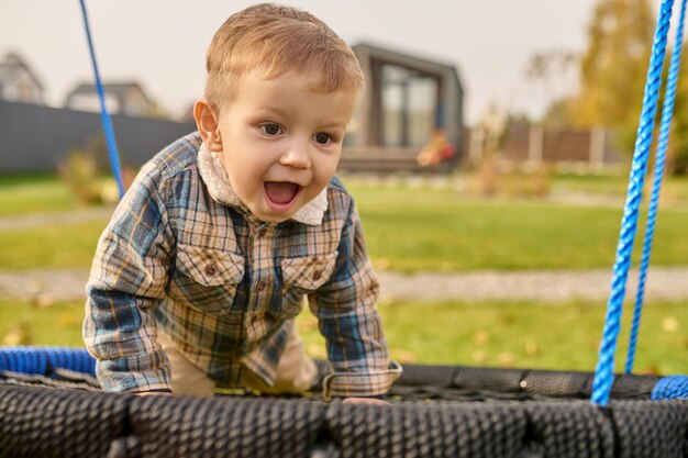 Enfant avec la bouche ouverte sur la balançoire près de la maison de campagne