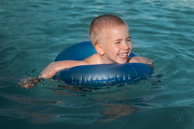 Enfant de coup moyen nageant avec une bouée de sauvetage