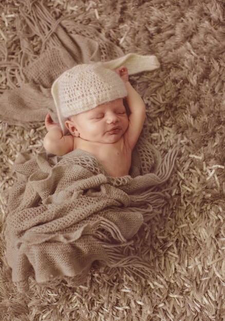 L&#39;enfant dans un chapeau comme des oreilles de lapin dort sur un tapis moelleux